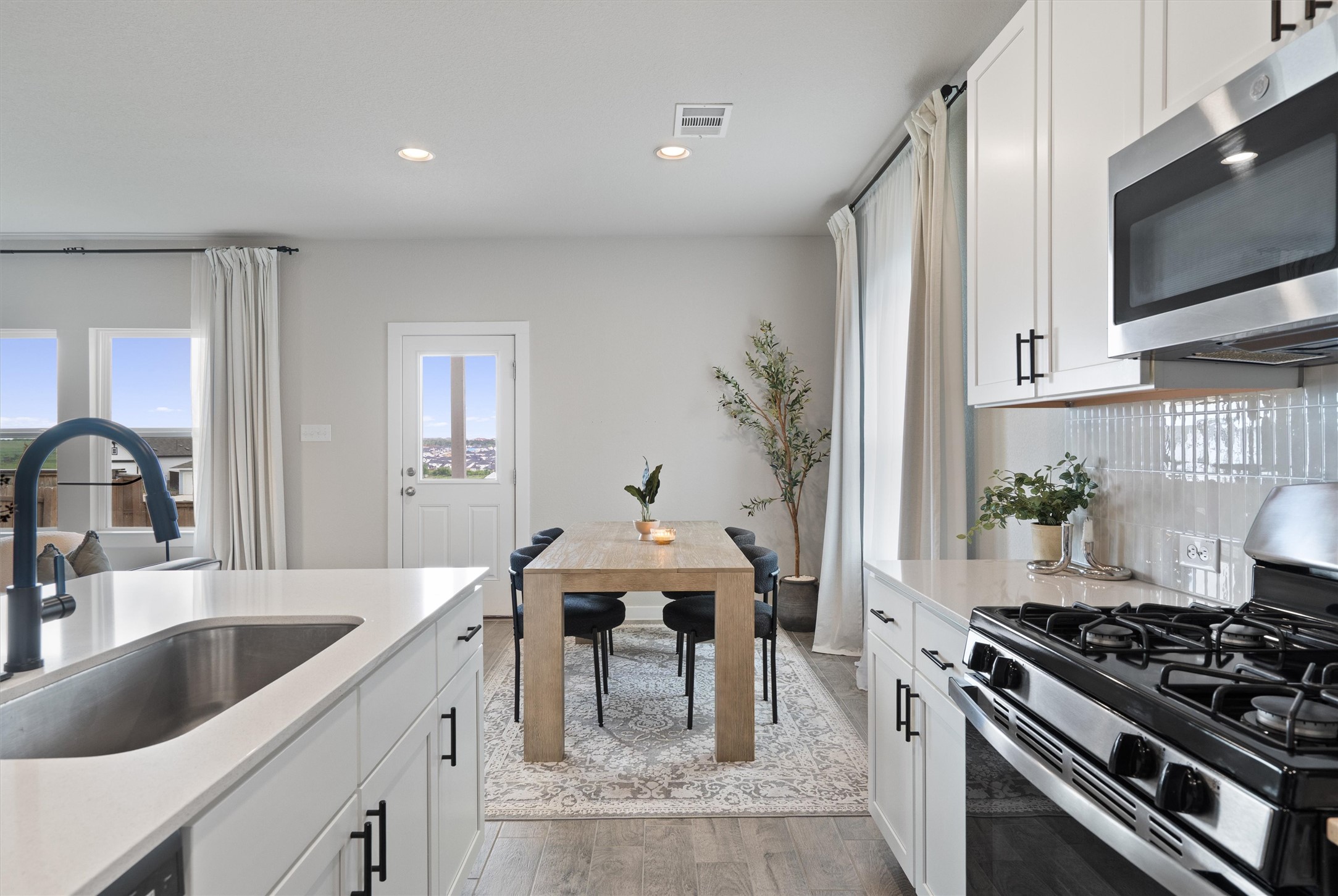 11620 Comano Drive Austin, TX 78747 - Photo 14 of 34 The kitchen features white cabinetry with black hardware, stainless steel appliances, and a counter-depth sink with a gooseneck faucet