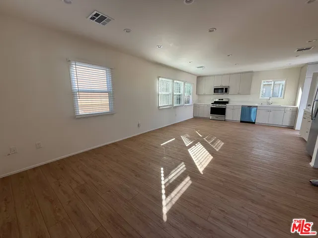 an empty room with wooden floor kitchen view and windows