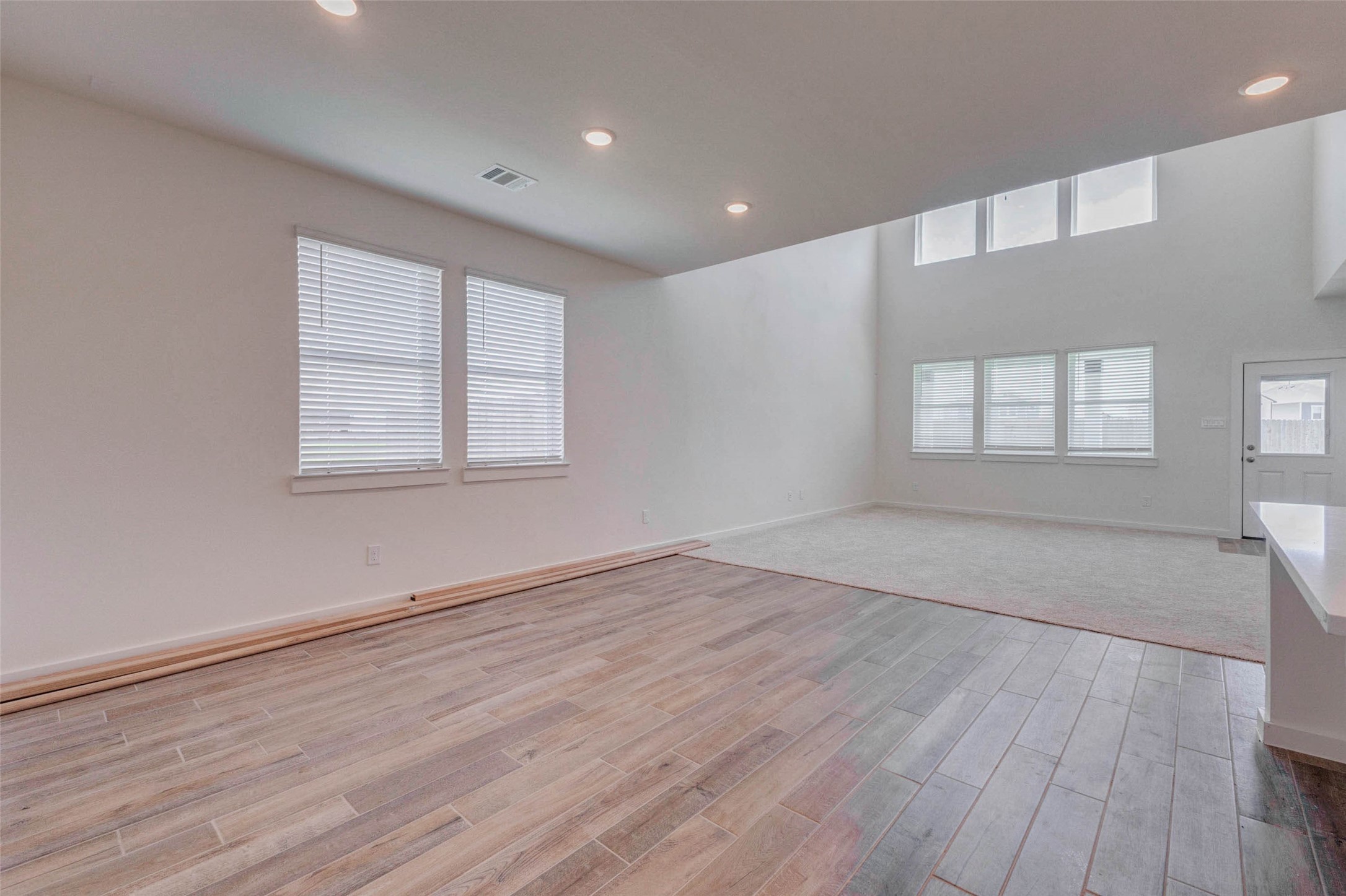 1206 Hemet Court Rosharon, TX 77583 - Photo 5 of 21 Open main living area with wood-look tile flooring, recessed lighting, tall ceilings, and abundant natural light. The layout transitions from dining or kitchen space into the spacious family room, creating an easy flow for daily living and entertaining. High windows add architectural interest and help brighten the room while maintaining a clean, open feel.