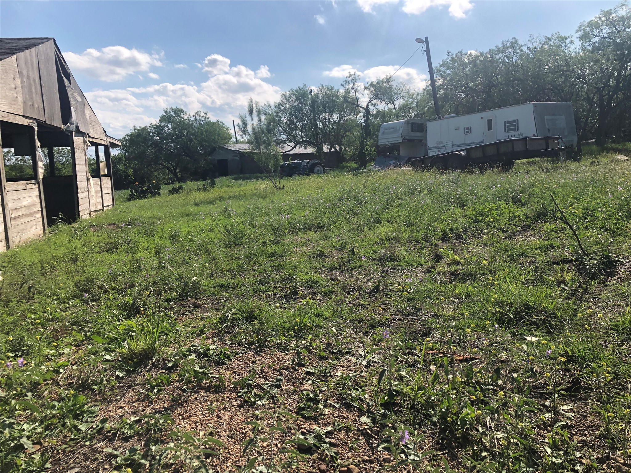 13414 Elm Grove Road Buda, TX 78610 - Photo 3 of 13 A rustic barn and trailers stand amidst a lush, verdant yard under a bright sky.