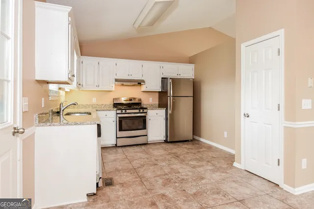 a kitchen with a refrigerator a stove top oven and white cabinets