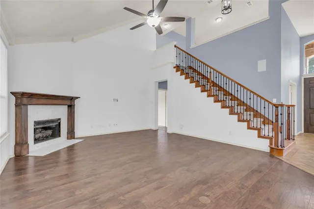 a view of an empty room with wooden floor a ceiling fan and a fireplace