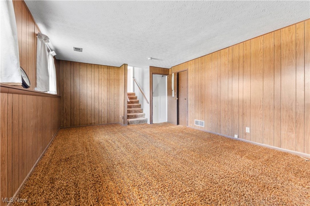 4301 Baird Road Stow, OH 44224 - Photo 32 of 50 Carpeted spare room with wood walls, stairs, visible vents, and a textured ceiling