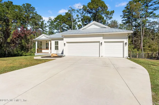 a view of a white house with a large tree and plants
