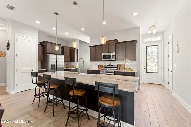 a kitchen with stainless steel appliances granite countertop a stove top oven a refrigerator a sink and chairs