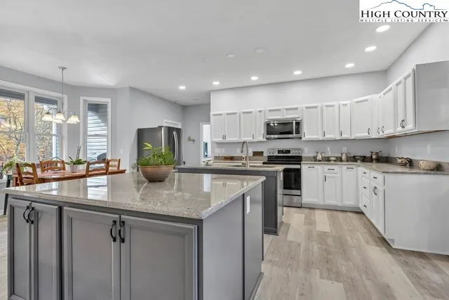 a kitchen with stainless steel appliances granite countertop a stove top oven a sink a refrigerator and white cabinets with wooden floor