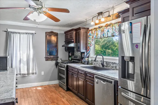 a kitchen with stainless steel appliances granite countertop a sink a counter space wooden floor and a window