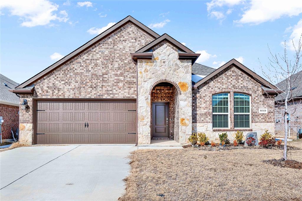 French country inspired facade with brick siding, stone siding, concrete driveway, and a garage