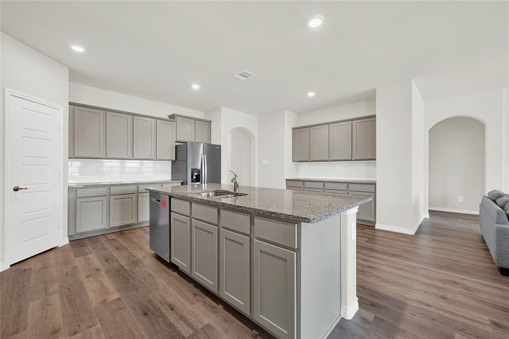 9713 Quail Pointe Road Aubrey, TX 76227 - Photo 8 of 23 Kitchen with arched walkways, decorative backsplash, gray cabinets, a kitchen island with sink, and light stone countertops