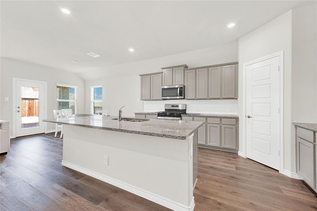 9713 Quail Pointe Road Aubrey, TX 76227 - Photo 9 of 23 Kitchen featuring gray cabinetry, stainless steel appliances, light stone countertops, a kitchen island with sink, and dark wood-style floors