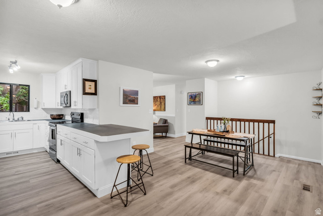 1539 East 450 South Springville, UT 84663 - Photo 21 of 49 Open-concept kitchen and dining area featuring white cabinetry, dark countertops, a kitchen island with seating, a white subway tile backsplash, and light wood-finish flooring