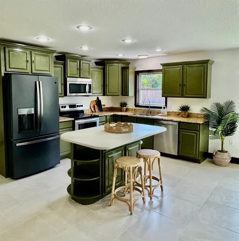 a kitchen with stainless steel appliances a sink a stove a refrigerator cabinets and a dining table