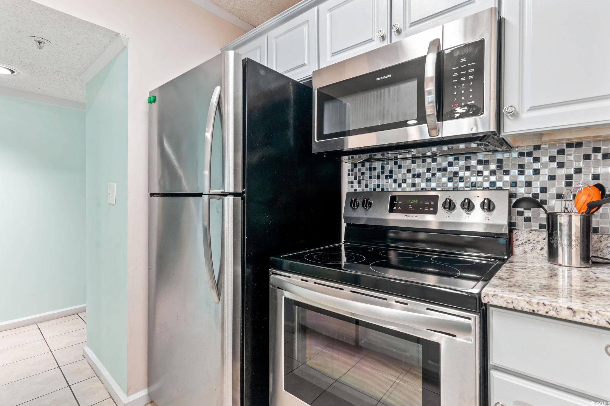 415 Ocean Creek Drive, Unit 2343 Myrtle Beach, SC 29572 - Photo 12 of 36 Kitchen featuring appliances with stainless steel finishes, a textured ceiling, tasteful backsplash, light tile patterned floors, and white cabinetry