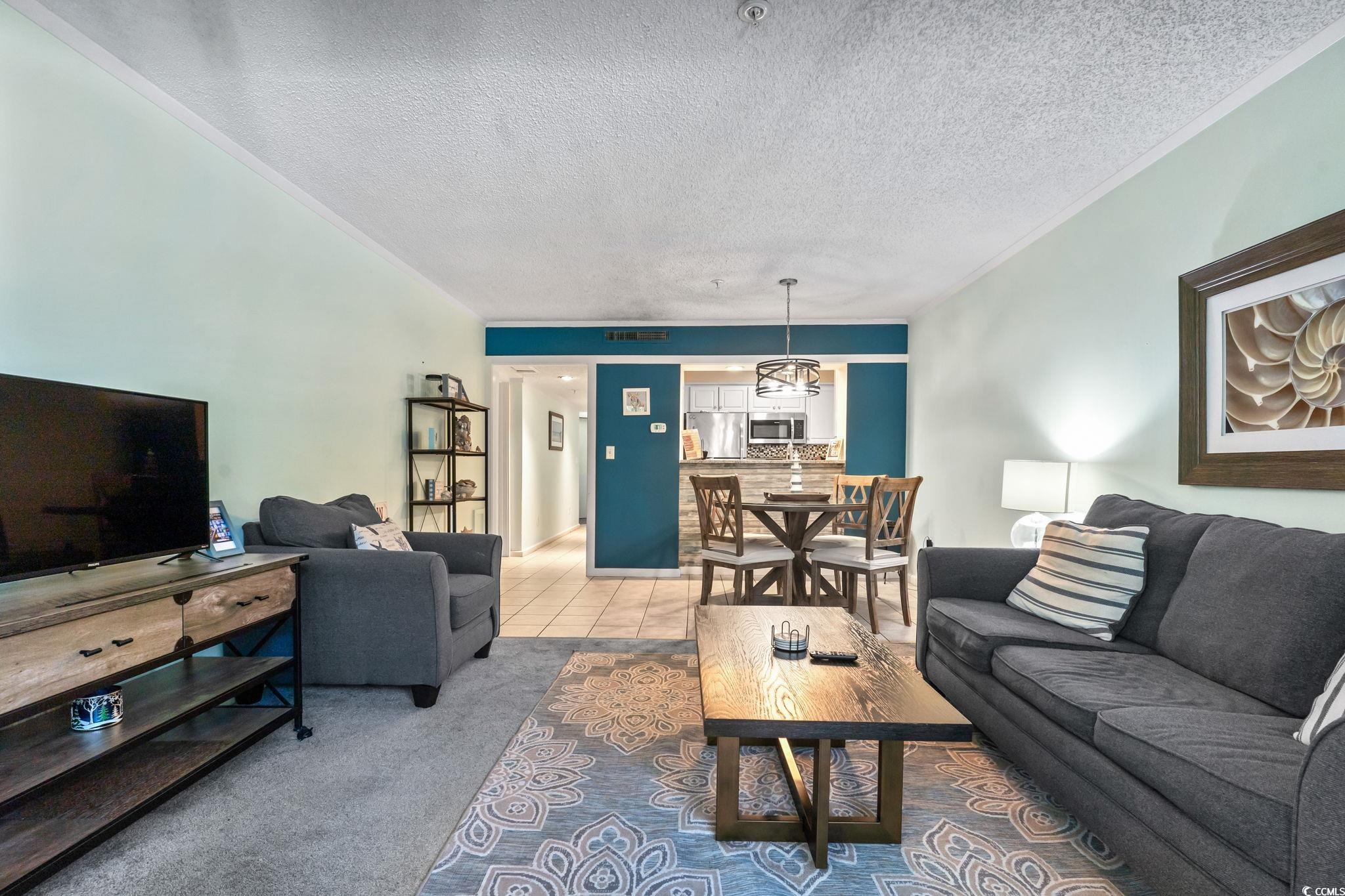 415 Ocean Creek Drive, Unit 2343 Myrtle Beach, SC 29572 - Photo 23 of 36 Carpeted living room featuring a textured ceiling, ornamental molding, and tile patterned flooring