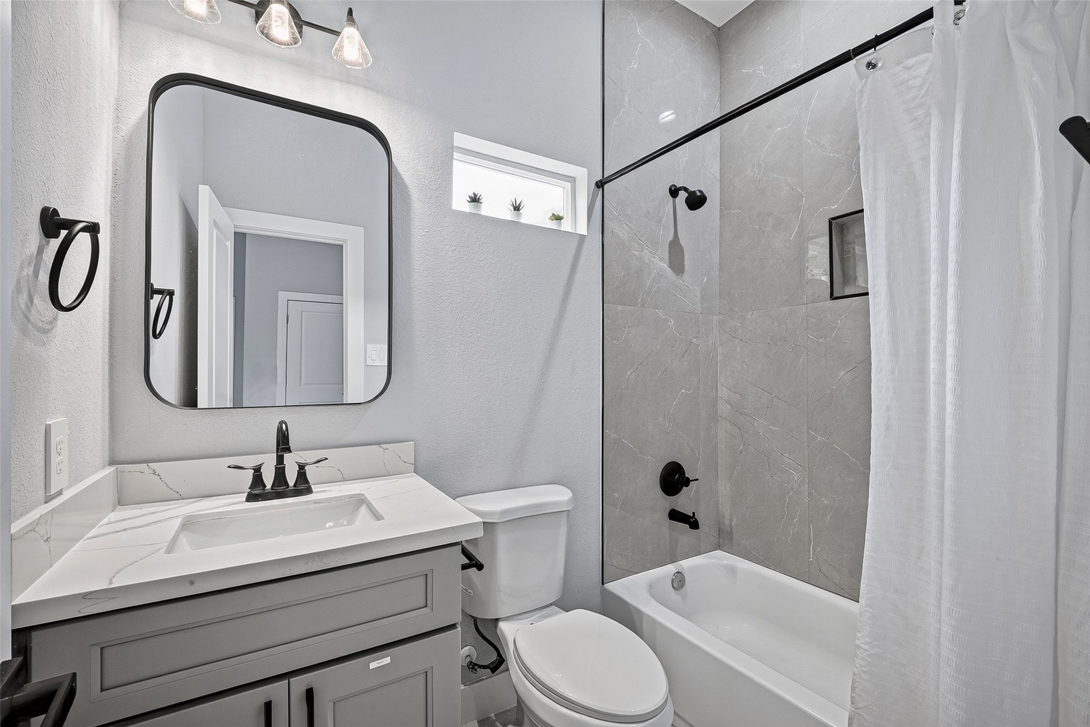 5027 Dickens Road, Unit B Houston, TX 77021 - Photo 22 of 24 Full bath with gray Shaker vanity, quartz countertop, matte-black mirror, and tiled tub/shower surround.