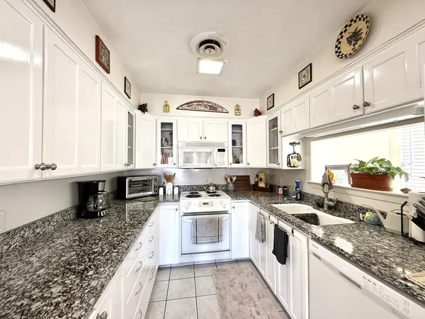 a large white kitchen with stainless steel appliances granite countertop a stove a sink and white cabinets