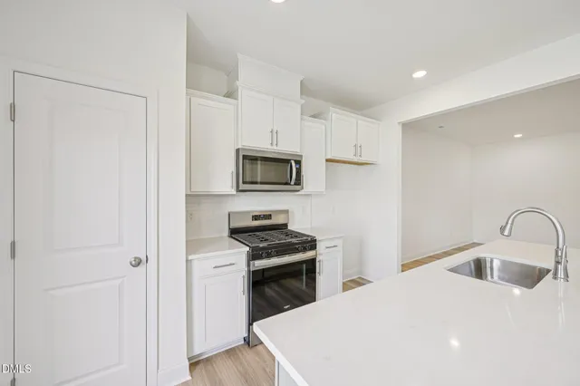 a kitchen with stainless steel appliances a stove a sink a refrigerator white cabinets and wooden floor