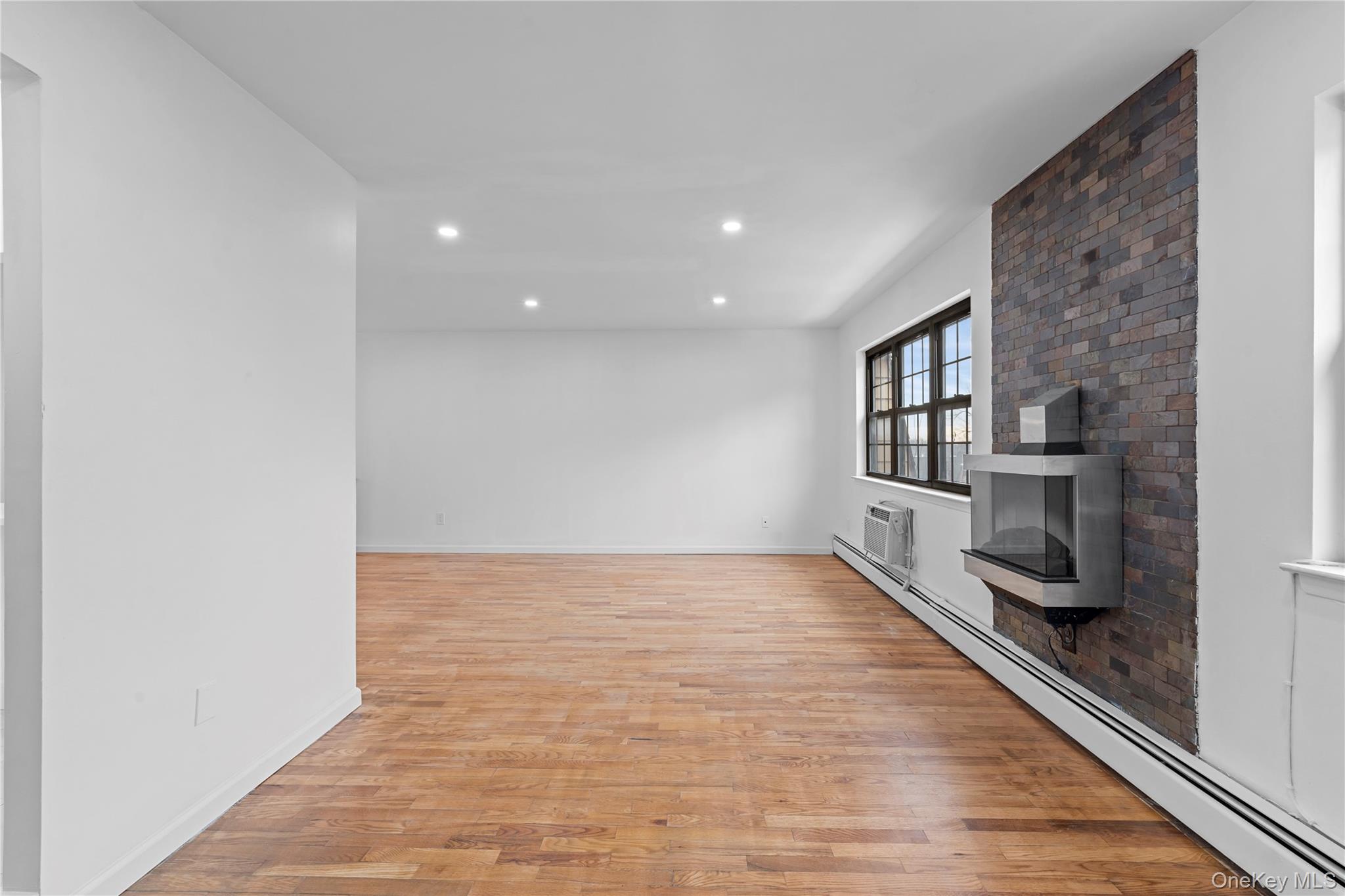 84-30 98th Street Queens, NY 11421 - Photo 11 of 35 Unfurnished living room with a baseboard heating unit, light wood-style flooring, recessed lighting, a fireplace, and a wall unit AC