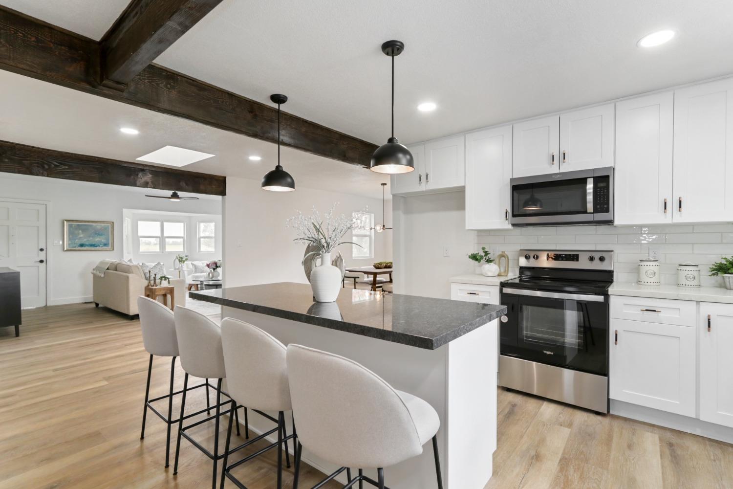 a kitchen with stainless steel appliances kitchen island granite countertop a stove a sink a microwave a dining table and chairs with wooden floor