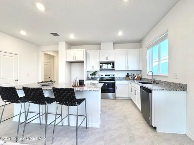 a kitchen with stainless steel appliances kitchen island granite countertop a stove top oven a sink a dining table and chairs