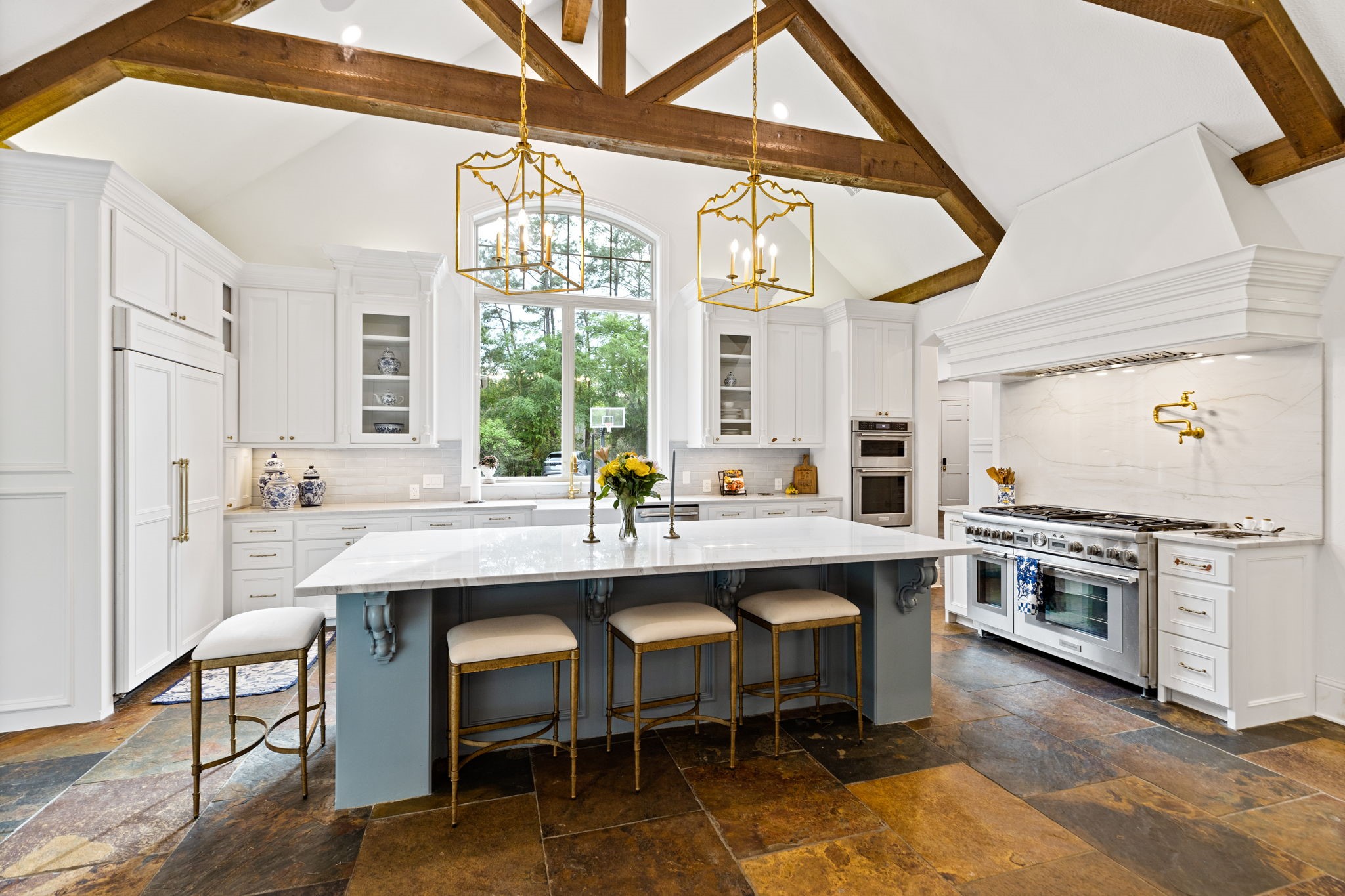 38223 Windy Ridge Trail Magnolia, TX 77355 - Photo 13 of 48 This remodeled kitchen features a spacious, open layout with high ceilings and exposed wooden beams. It includes a large central Quartz island with bar seating for your bar stools, elegant white cabinetry, and modern appliances that include a built in refrigerator, Thermador range with two ovens & an extra oven on the adjacent wall to make 3, a warmer, Thermador dishwasher & a porcelain farmhouse sink. The space is brightened by natural light from a large window and highlighted by stylish pendant lighting.