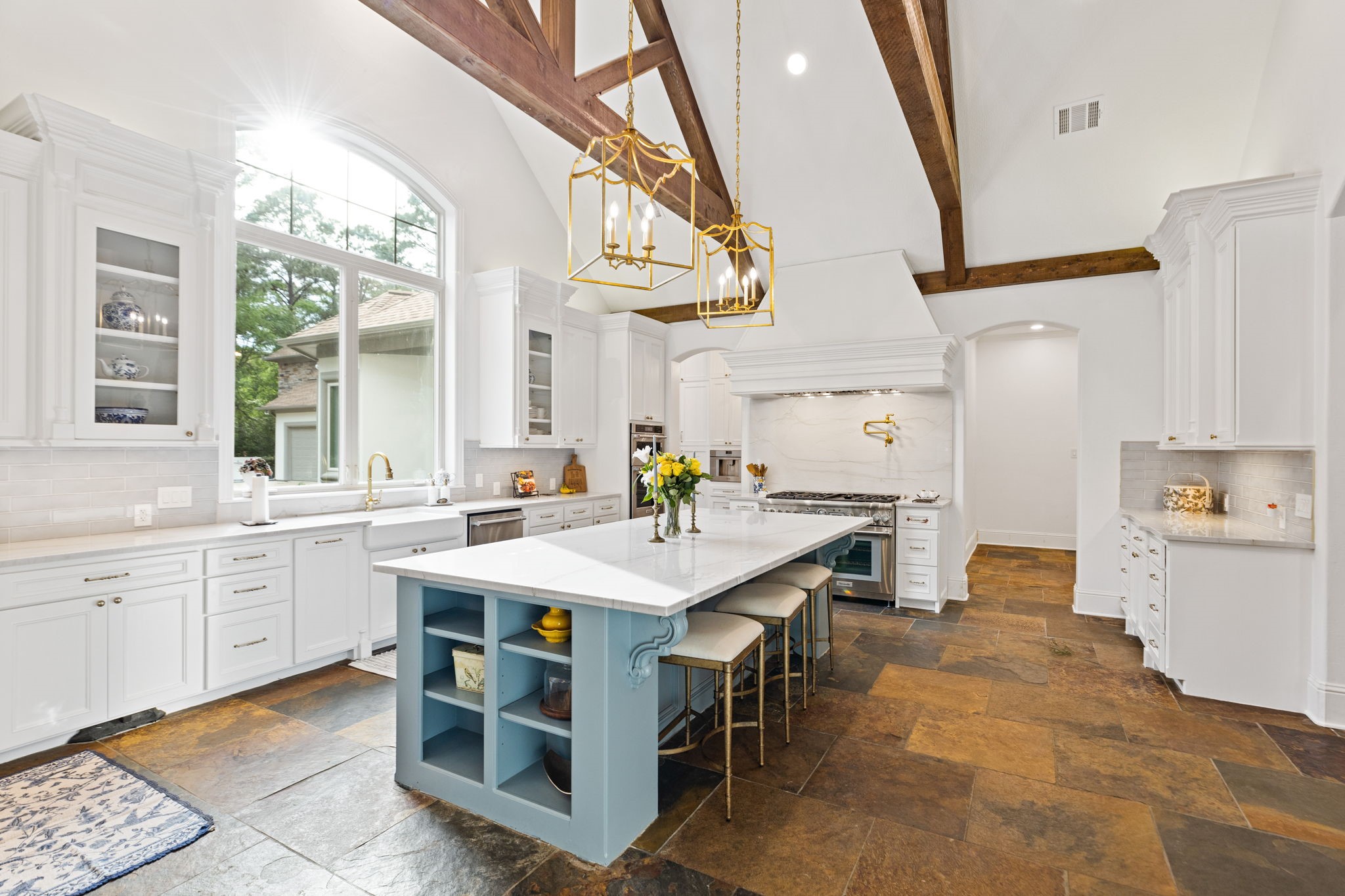 38223 Windy Ridge Trail Magnolia, TX 77355 - Photo 14 of 48 This spacious kitchen features high ceilings with exposed wooden beams, a large central island with extra shelves. Plenty of cabinets for your kitchen storage. Natural light streams through a large arched window, highlighting the open and airy design.