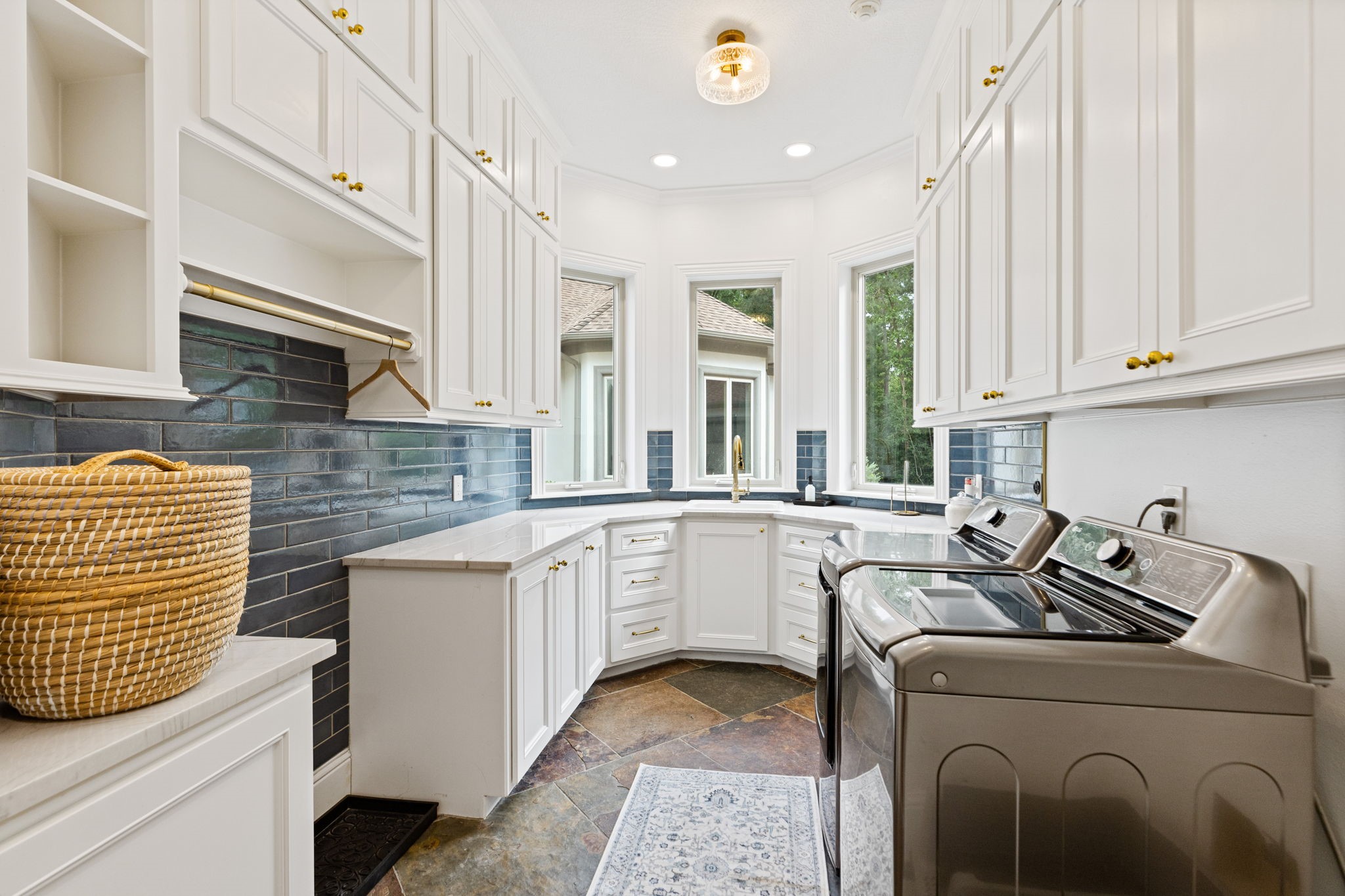 38223 Windy Ridge Trail Magnolia, TX 77355 - Photo 19 of 48 This photo showcases a bright, elegant laundry room with ample white cabinetry, subway tile backsplash, and large windows providing natural light. It features spacious countertops for doing your laundry chores, perfect for organization and functionality.