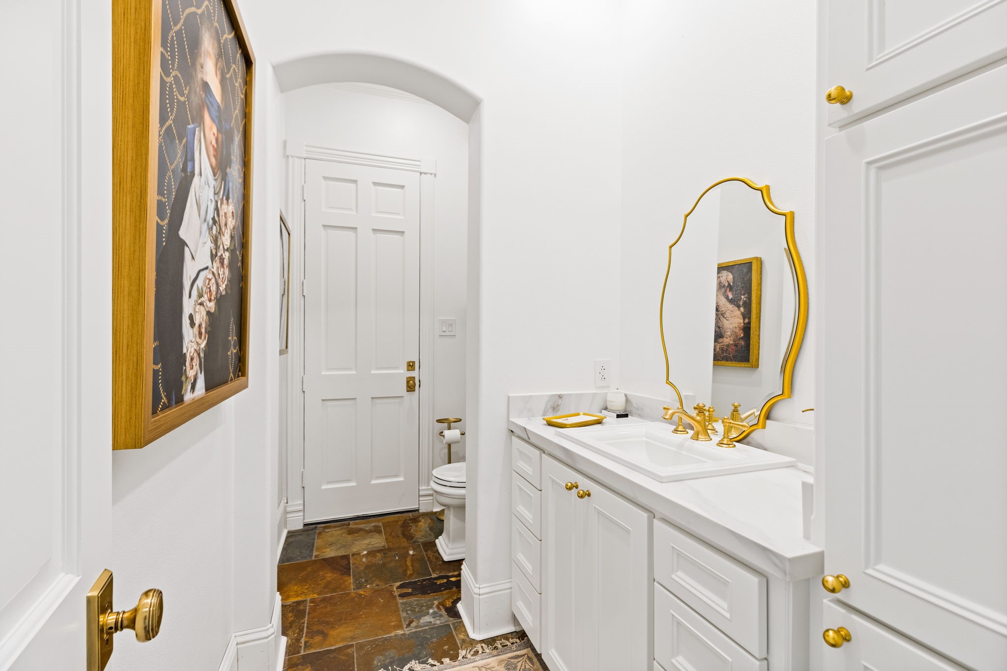 38223 Windy Ridge Trail Magnolia, TX 77355 - Photo 27 of 48 This remodeled pool bath features elegant white cabinetry with gold hardware, a stylish gold-framed mirror, and a classic sink. The slate tile floor adds character and enhances the space's sophistication.