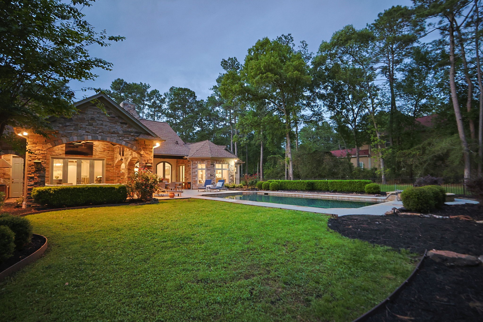 38223 Windy Ridge Trail Magnolia, TX 77355 - Photo 40 of 48 This beautiful property features a spacious stone house with large windows and a well-maintained lawn. The backyard offers a serene pool area surrounded by lush greenery, perfect for relaxation and entertaining.