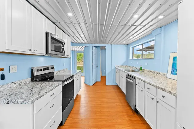 a large kitchen with stainless steel appliances granite countertop a large stove a sink dishwasher and white cabinets with wooden floor