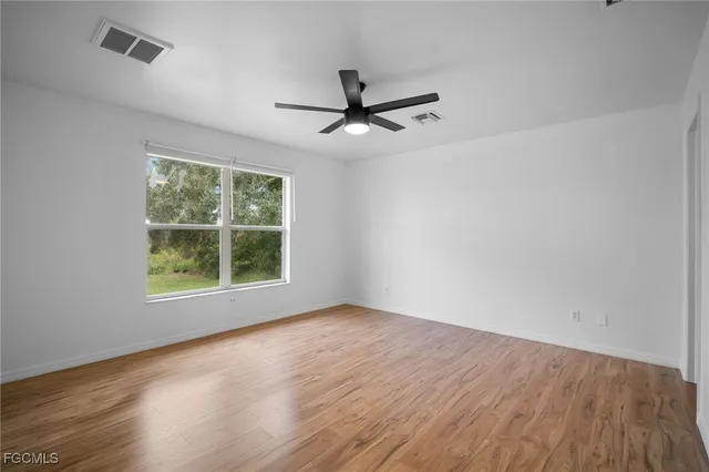 an empty room with wooden floor fan and windows
