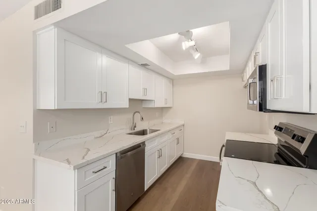 a kitchen with a sink dishwasher and white cabinets with wooden floor