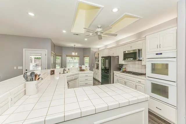 a large kitchen with kitchen island a stove a sink a refrigerator and a dining table with wooden floor