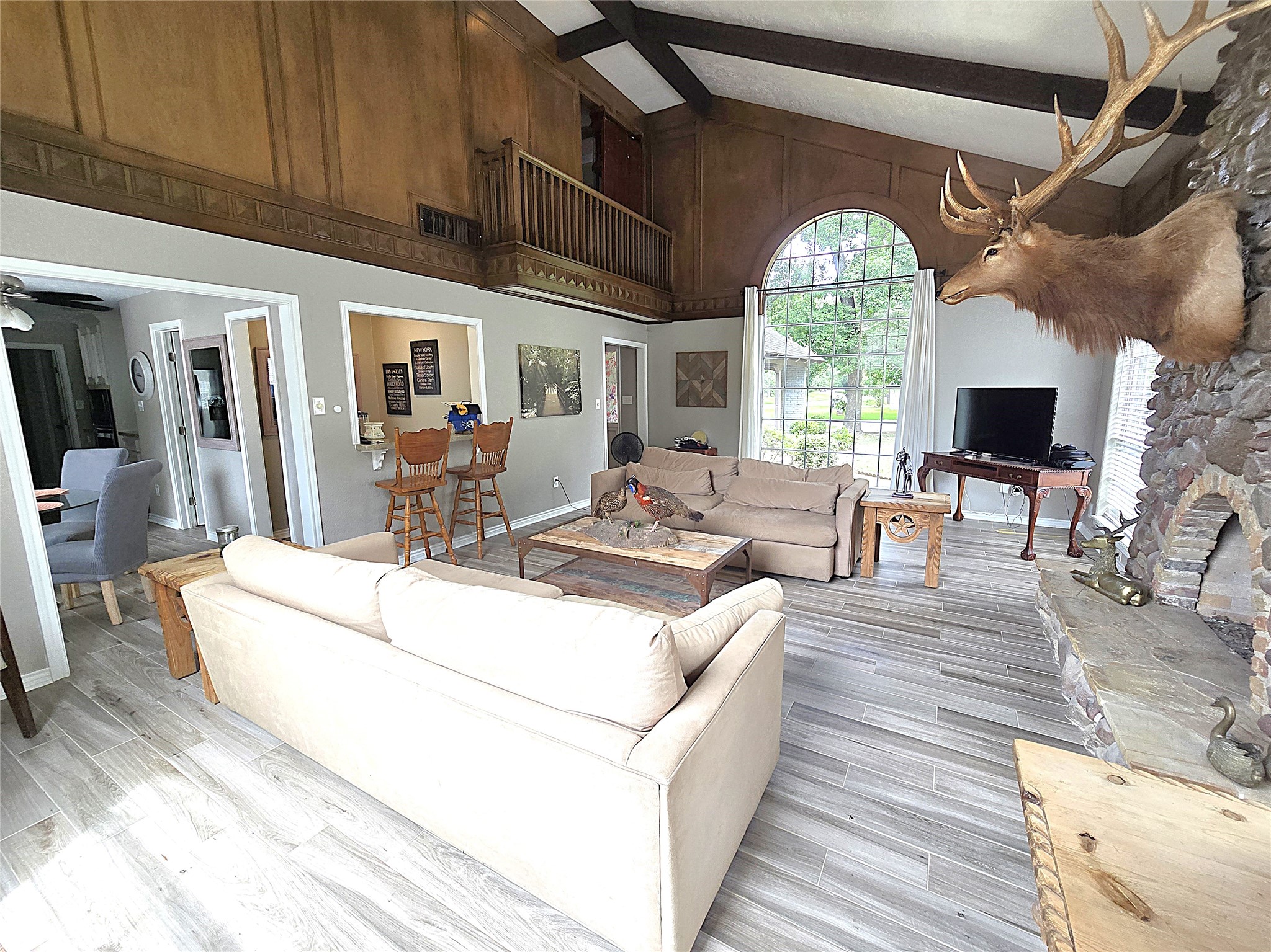 560 Brandon Road Conroe, TX 77302 - Photo 33 of 45 This inviting living room features soaring ceilings, abundant natural light from large windows, and a rustic stone fireplace, creating a warm and spacious atmosphere perfect for relaxation and entertaining.