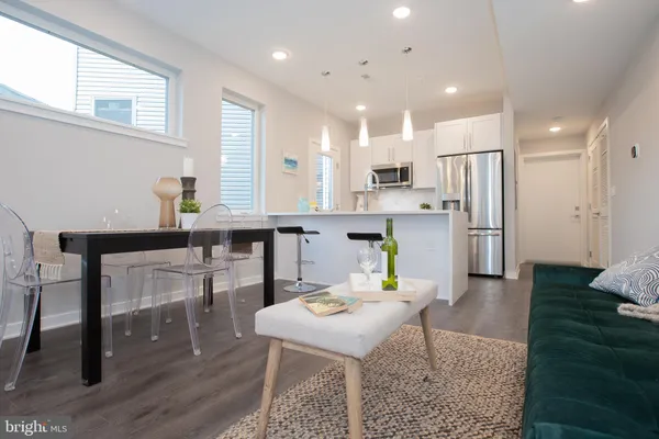 a open kitchen with stainless steel appliances kitchen island granite countertop a dining table chairs and a refrigerator