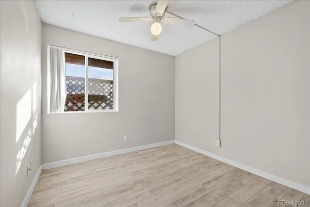 an empty room with wooden floor fan and windows
