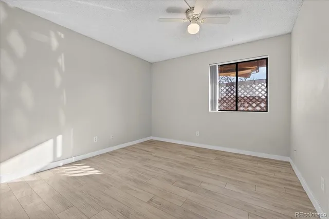 a view of an empty room with wooden floor and a ceiling fan