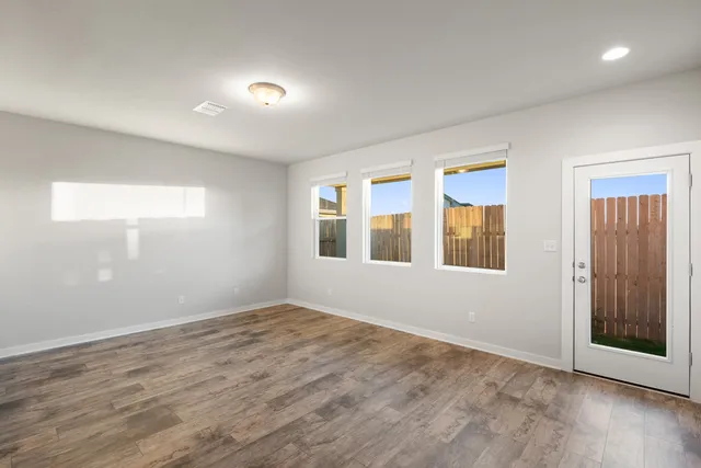 a view of an empty room with wooden floor and windows