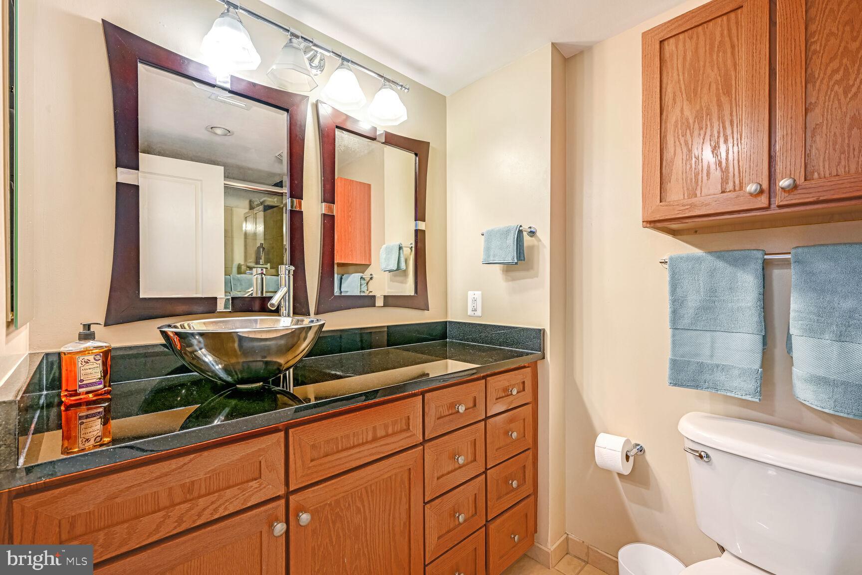 616 E Street Northwest, Unit 1150 Washington, DC 20004 - Photo 23 of 75 a bathroom with a granite countertop sink a toilet a mirror and shower