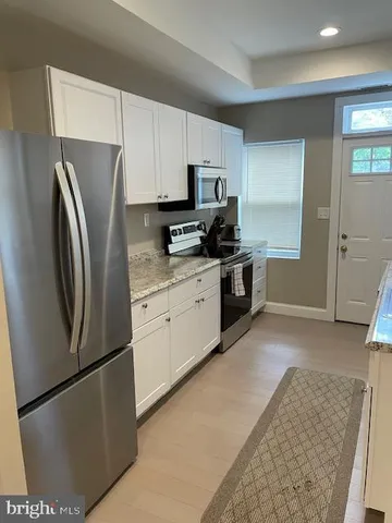 a kitchen with stainless steel appliances granite countertop a refrigerator a stove a sink and white cabinets