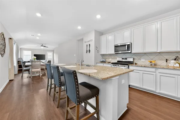 a kitchen with stainless steel appliances kitchen island granite countertop a table chairs sink and cabinets