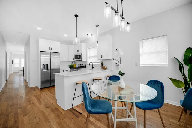 a kitchen with stainless steel appliances kitchen island granite countertop a dining table chairs and a refrigerator