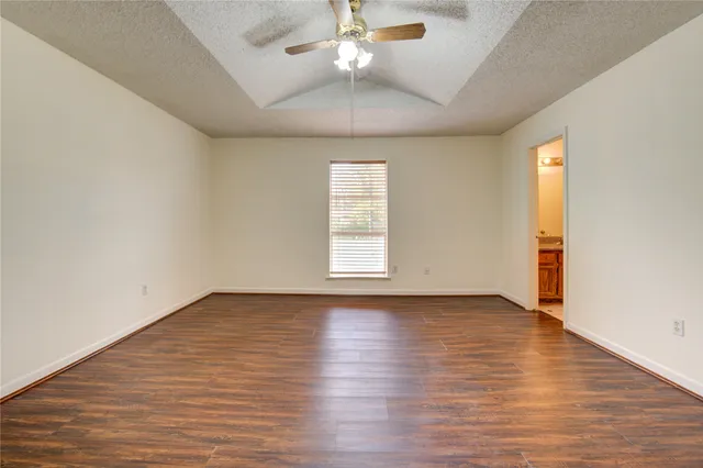 an empty room with wooden floor chandelier fan and windows