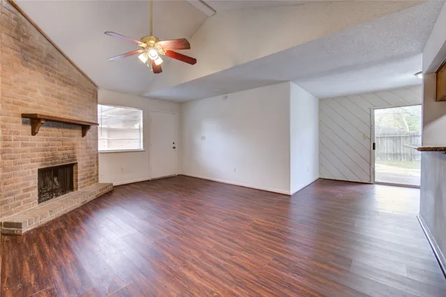 a view of an empty room with wooden floor fireplace and a window
