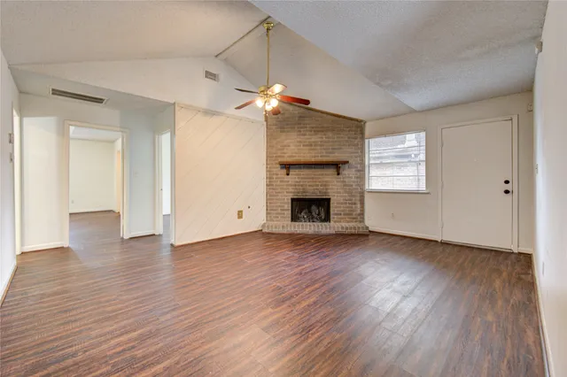 an empty room with wooden floor fireplace and windows