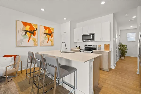 a kitchen with stainless steel appliances a stove a sink a refrigerator and a dining table with wooden floor