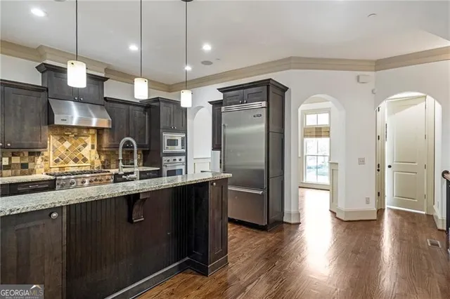 a kitchen with stainless steel appliances granite countertop a refrigerator a sink a stove and wooden floors