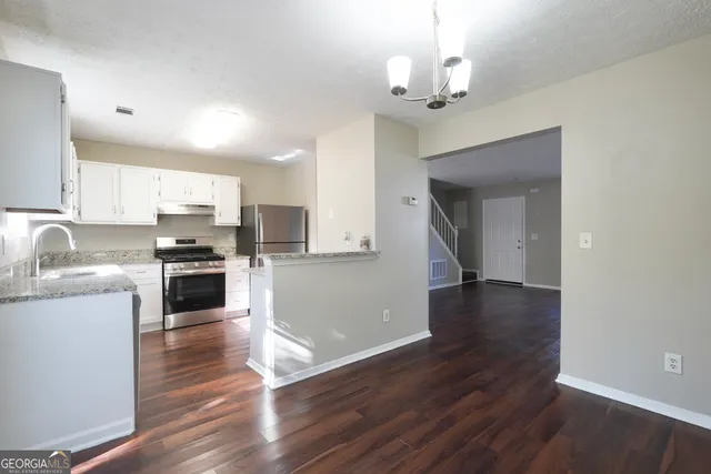 a kitchen with granite countertop a refrigerator oven a sink dishwasher and white cabinets with wooden floor