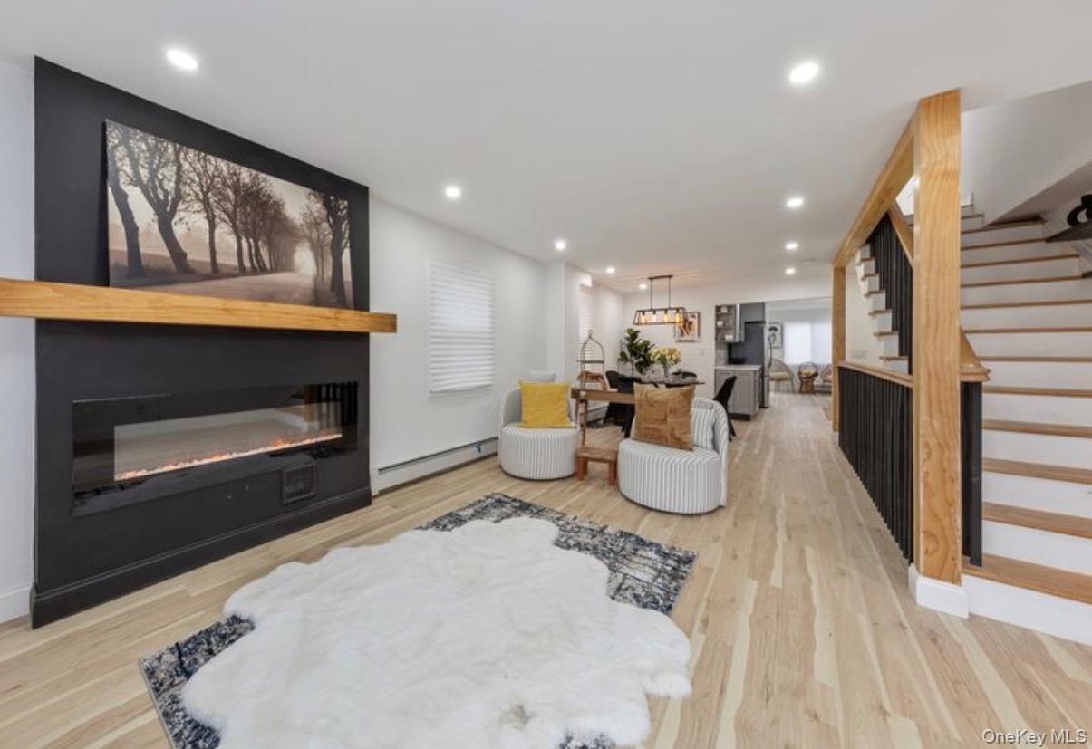 136-18 221st Street Queens, NY 11413 - Photo 3 of 23 Living area with a glass covered fireplace, a baseboard radiator, stairway, recessed lighting, and light wood-style flooring