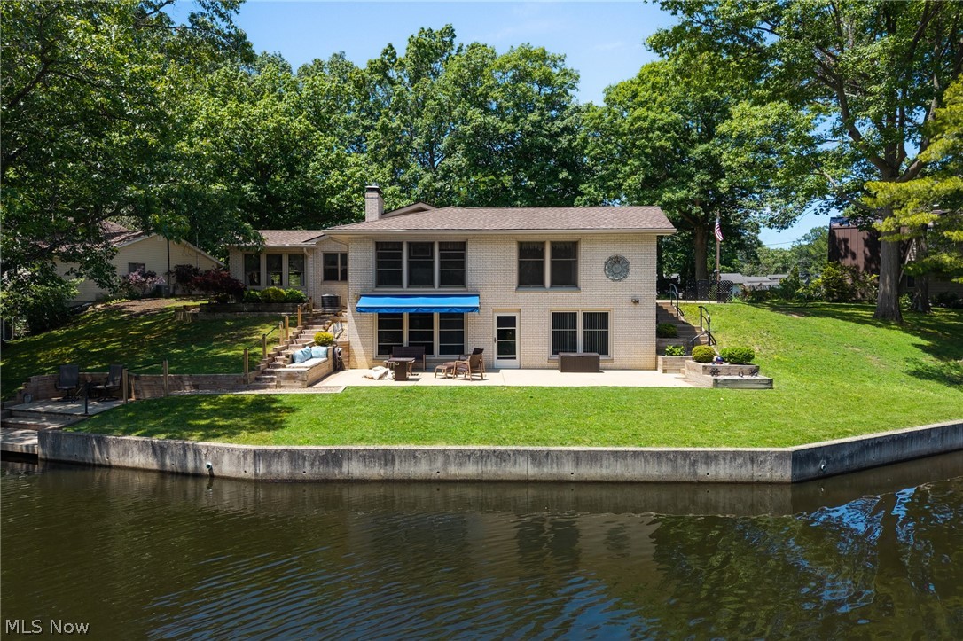 685 Sunnyside Road Vermilion, OH 44089 - Photo 45 of 50 Waterfront property featuring a stone patio, terraced landscaping, a blue retractable awning, and mature trees